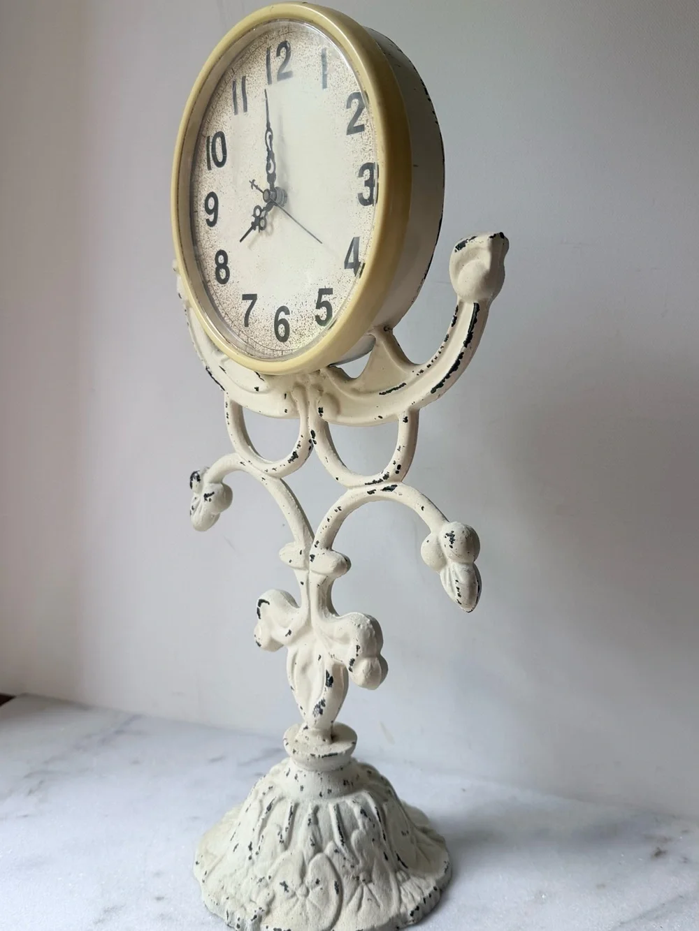 This vintage-style table clock features a distressed cream iron stand